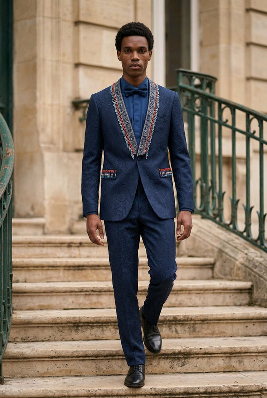 A man wearing a navy blue textured suit with ornate embroidered trim on the jacket lapels and pockets, walking down stone stairs.