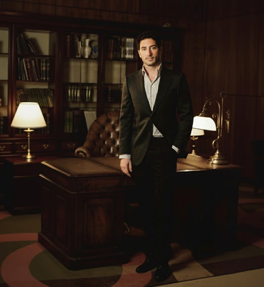 A man wearing a navy two-piece suit with a notched lapel, standing in an office setting.
