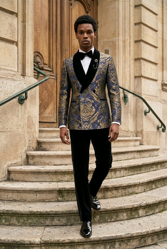 A man wearing a patterned blue and gold tuxedo jacket with black velvet shawl collar, black trousers, and a black bow tie walks down stone steps in front of a classical building.