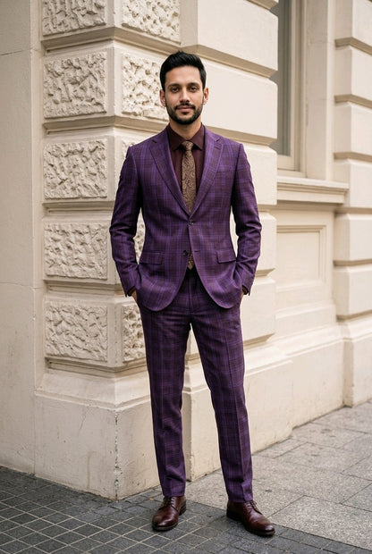 A man wearing a purple and brown plaid suit with a brown patterned tie and brown leather shoes, standing in front of a beige stone building corner.