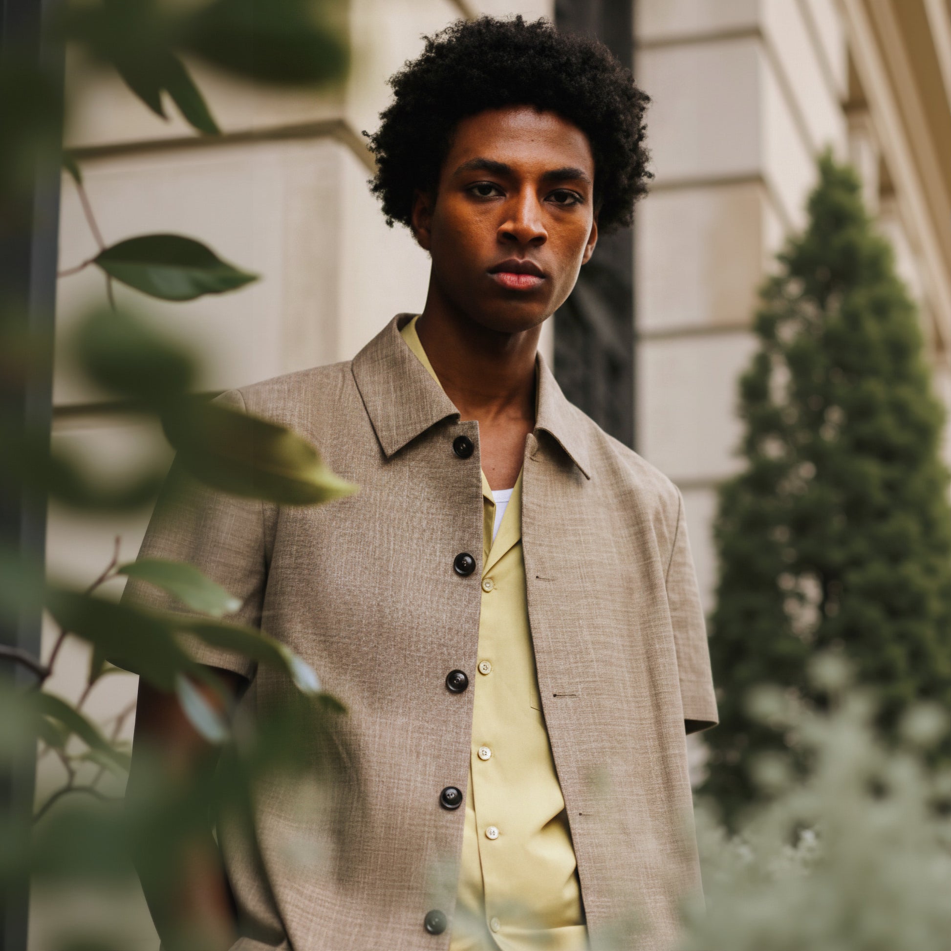 A man wearing a short-sleeved, button-up shirt in a sand color, with a collar, made of a blend of bamboo, spandex, silk, and wool fabrics.
