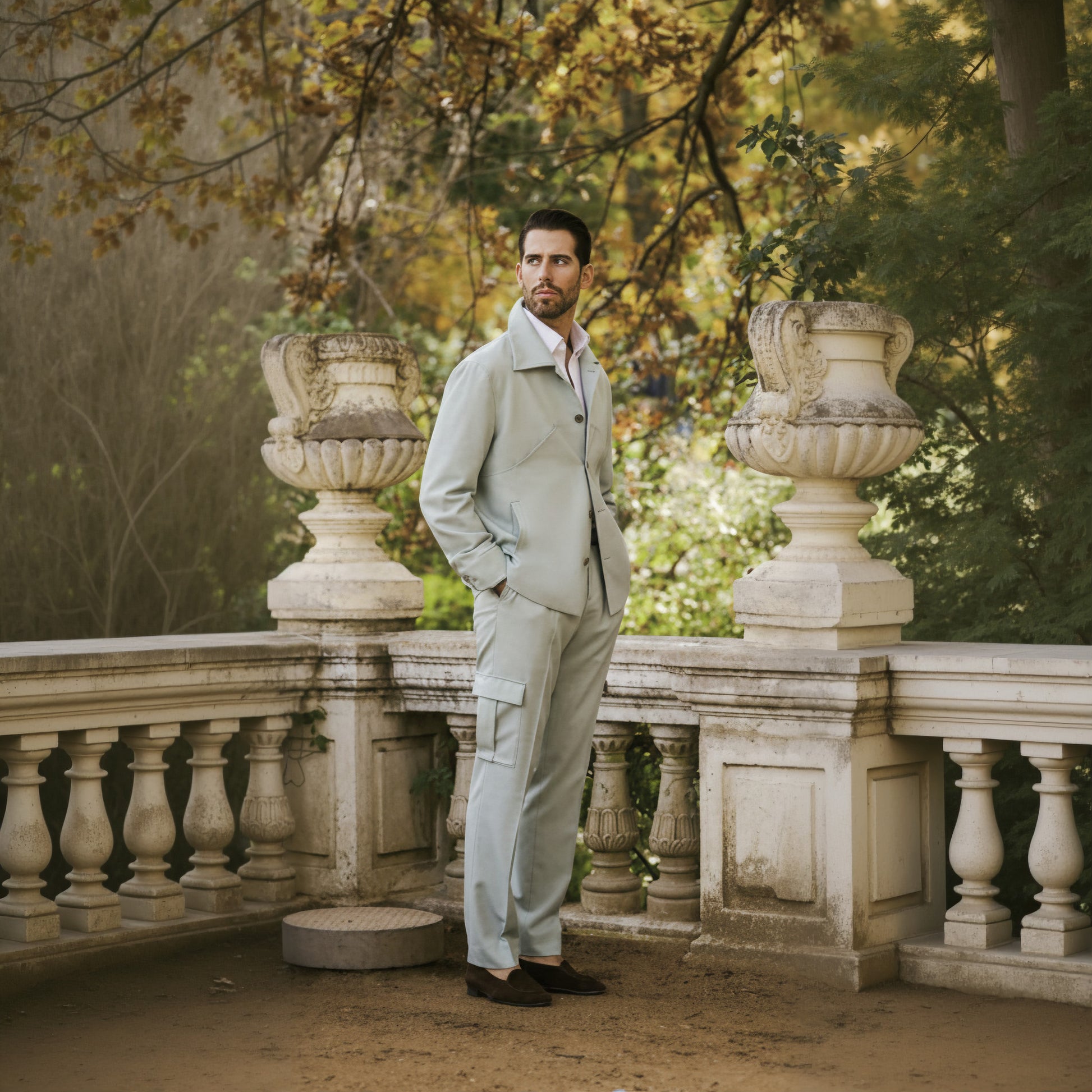 A man wearing a two piece Italian sage wool stretch suit with a shirt and tie, standing in front of a garden backdrop.