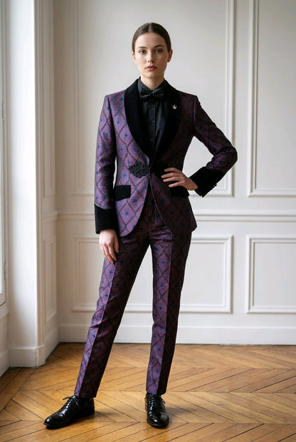 A model stands in a room with white paneled walls and a wooden parquet floor, wearing a purple and black patterned suit with a black shirt and bow tie.