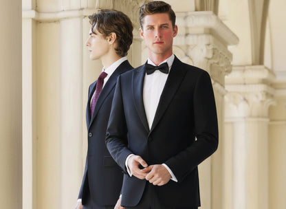 A model wearing a black tuxedo with a single-breasted jacket and gold brocade peak lapel, paired with black trousers.