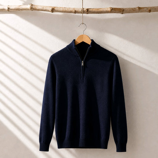 A navy blue half-zip knit sweater hanging on a wooden hanger from a rustic branch, set against a textured off-white wall with diagonal shadow patterns.