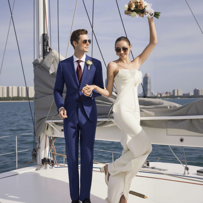 A navy herringbone single-breasted two-piece suit, with the jacket and trousers worn by a man and a woman, respectively, standing on a boat.
