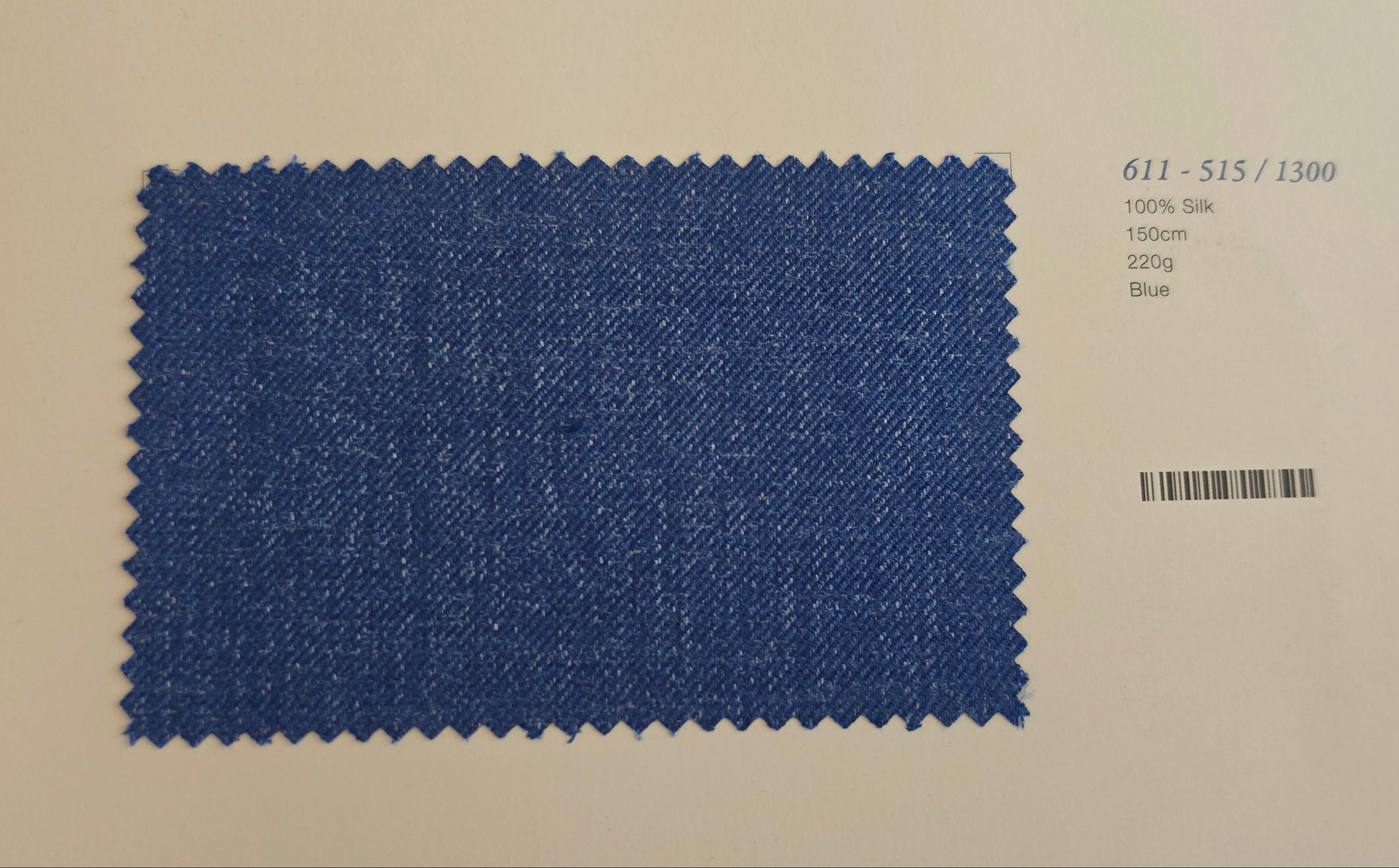A rectangular blue fabric swatch with zigzag-cut edges, shown on a white card with a barcode and small printed text below it.