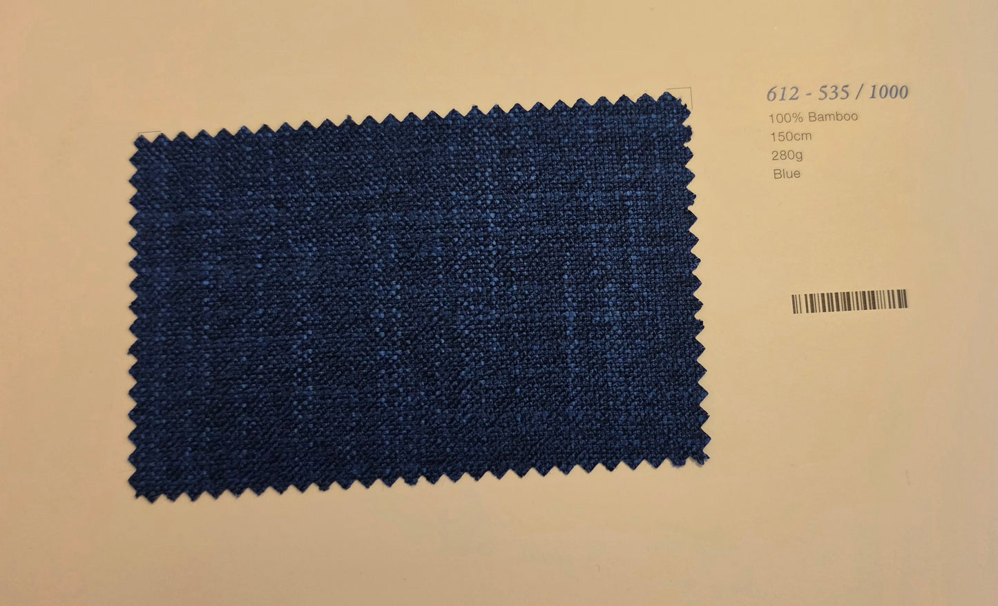 A rectangular fabric swatch of dark blue woven material with zigzag-cut edges, placed on a light beige background with printed text and a barcode to the right.