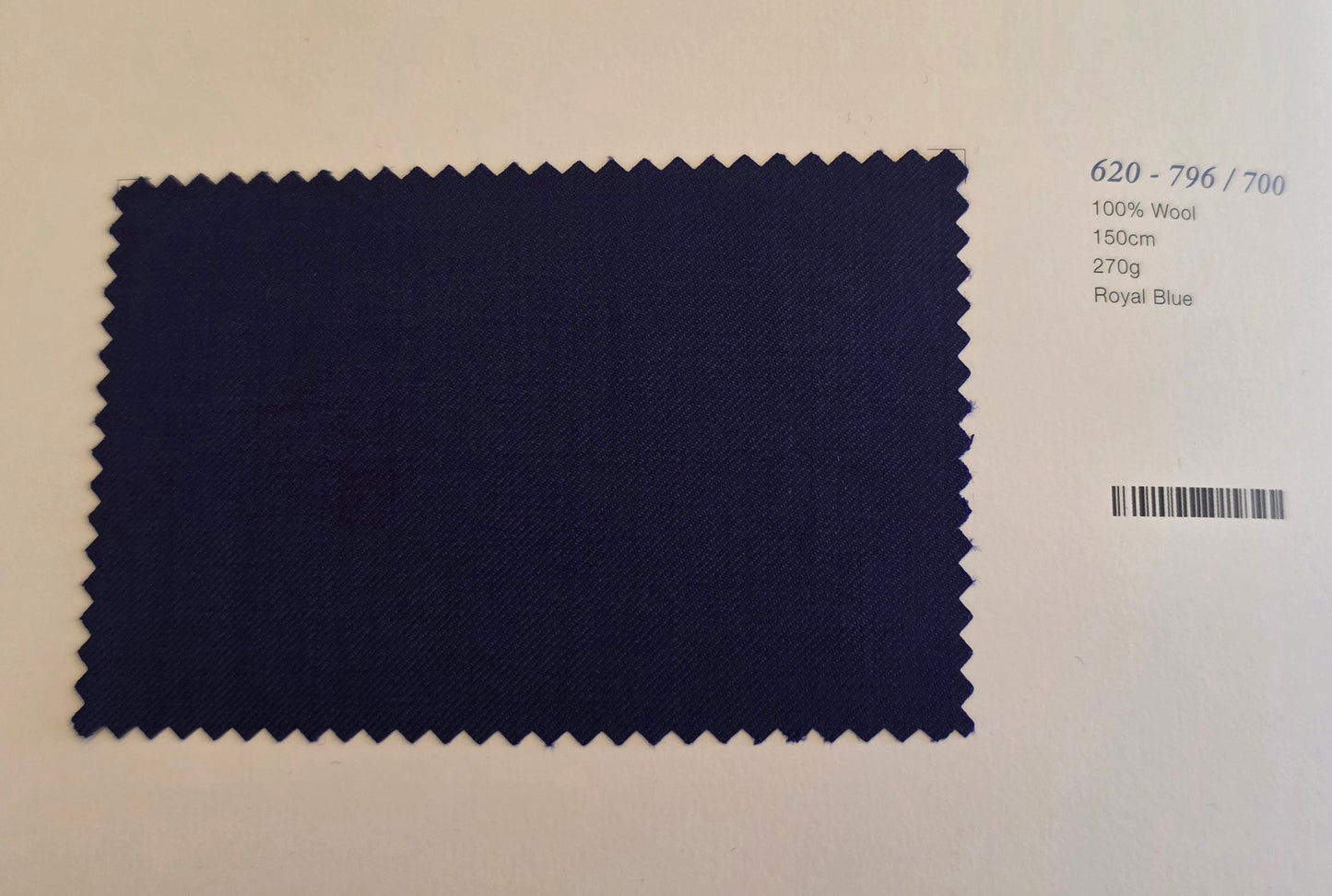A rectangular fabric swatch of dark royal blue wool with serrated edges, displayed on a light beige background with printed text details on the right.
