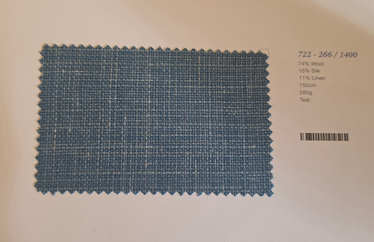 A rectangular fabric swatch of woven teal blue material with a scalloped cut edge, placed on a white background next to printed text showing composition and material details.