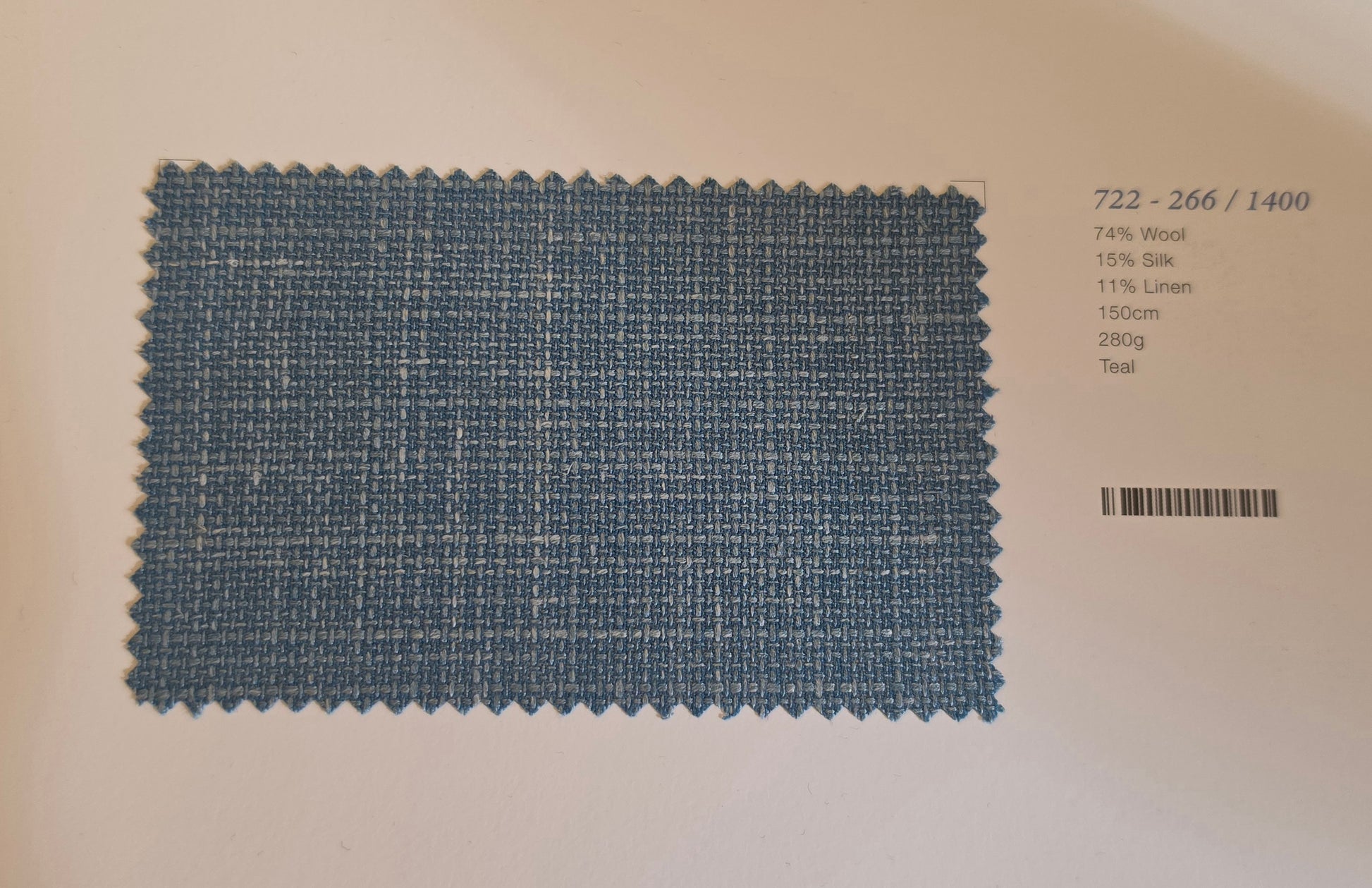 A rectangular fabric swatch of woven teal blue material with a scalloped cut edge, placed on a white background next to printed text showing composition and material details.