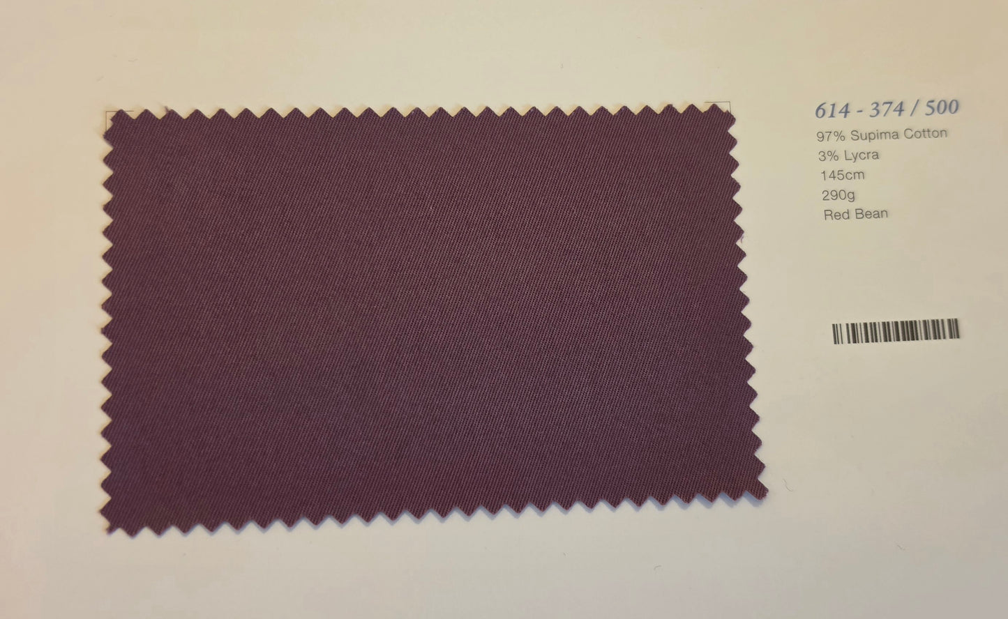 A rectangular fabric swatch with serrated edges in a muted burgundy-purple color, displayed on a white background with printed text and a barcode to the right.