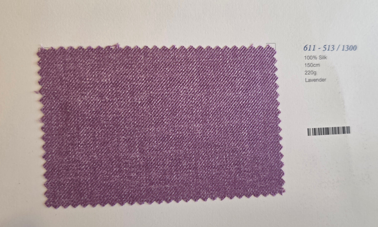 A rectangular lavender-colored fabric swatch with serrated edges, displayed on a white background next to printed text identifying the color and specifications.