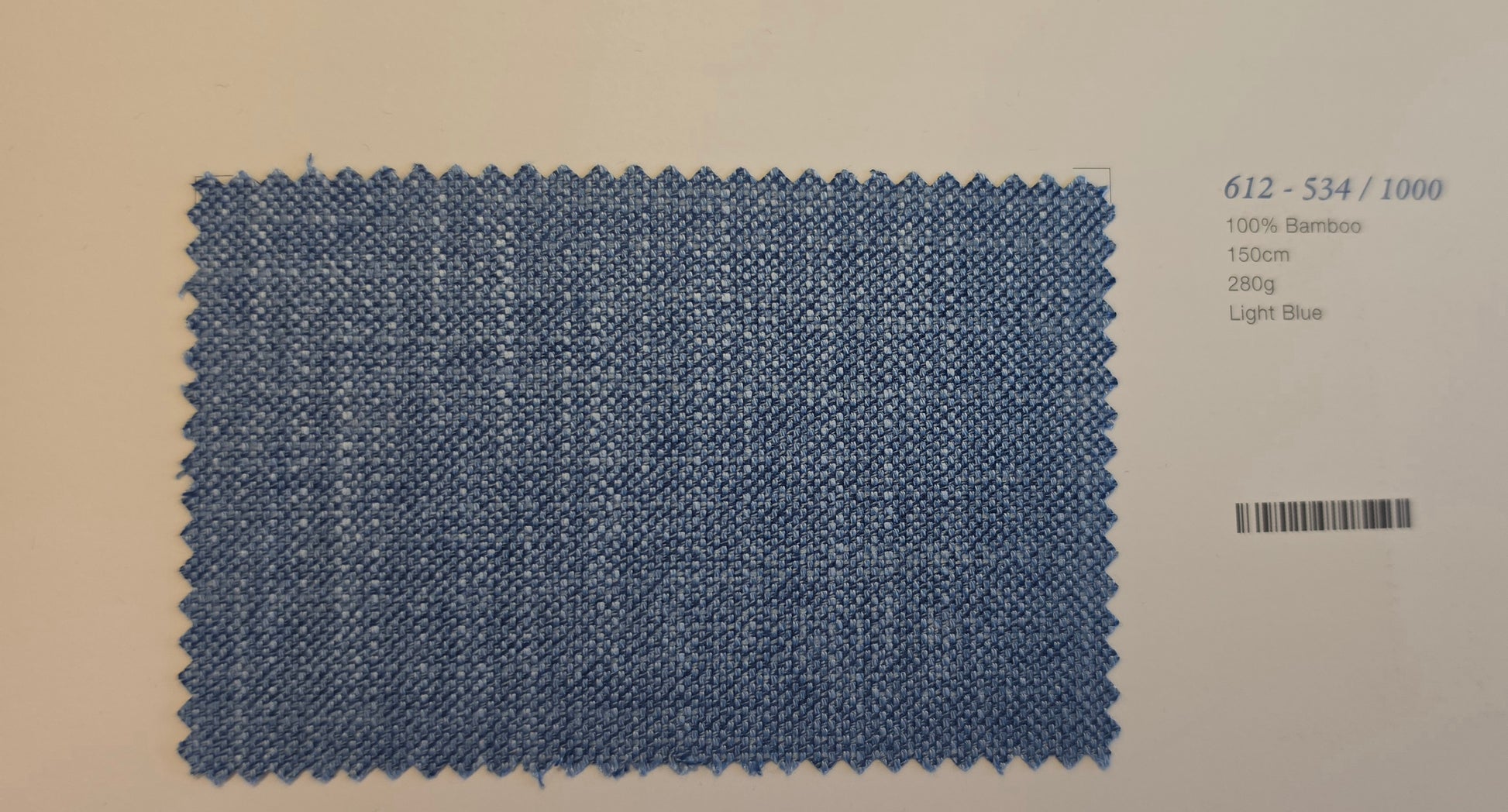A rectangular light blue bamboo fabric swatch with zigzag-cut edges, displayed on a light beige background with printed text details on the right.