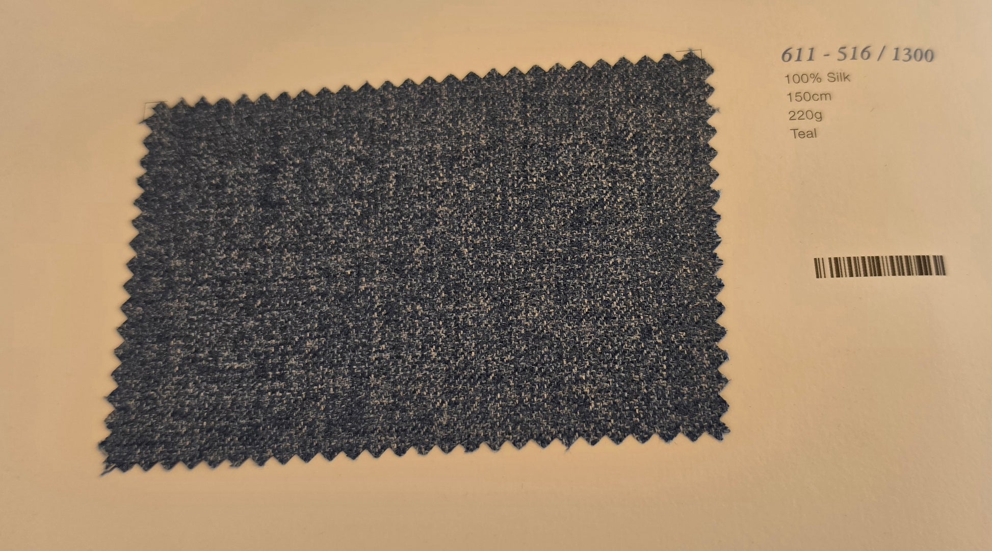 A square fabric swatch of teal woven material with zigzag-cut edges, placed on a beige background with printed text in the upper right showing code 611-516/1300, 100% silk, 150cm, 220g, and Teal.