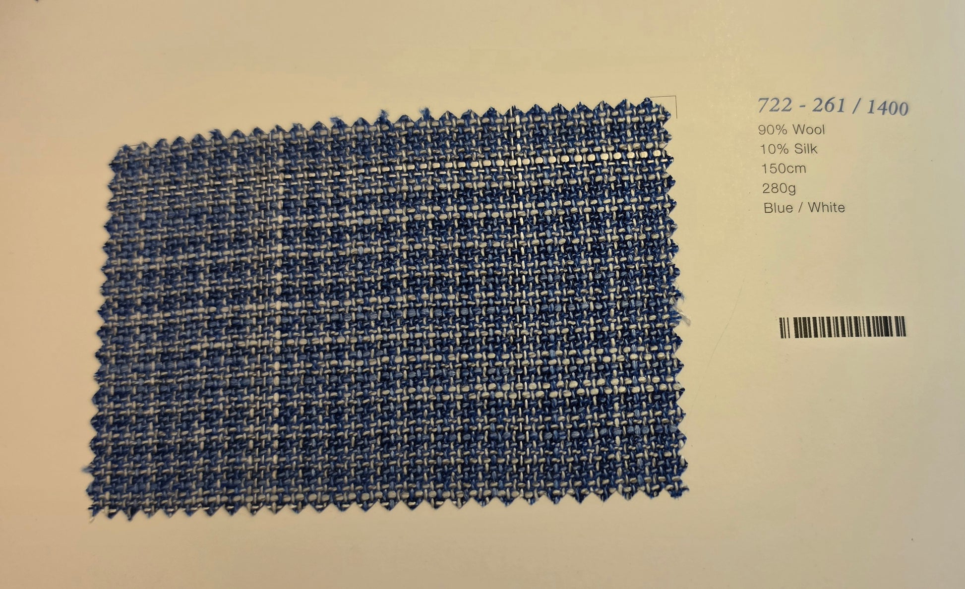 A square woven fabric swatch in blue and white, displayed on a light beige background with printed text and a barcode indicating material composition and color details.
