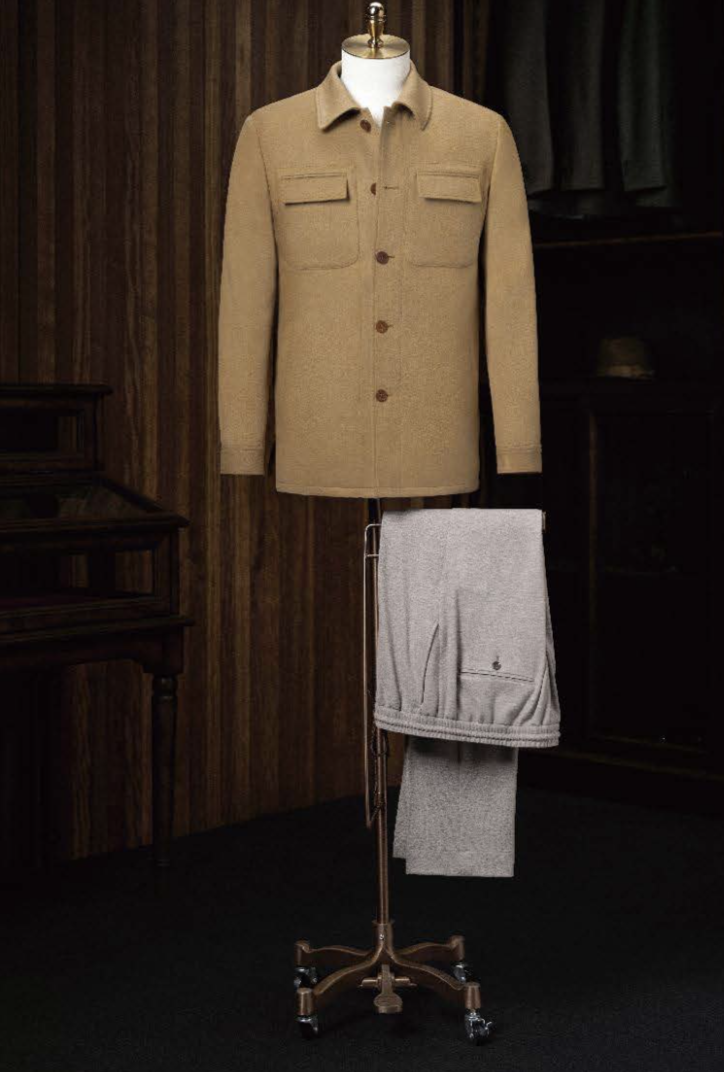 A tan camel casual jacket displayed on a mannequin with beige trousers, arranged on a wooden floor in a room with wooden panels.