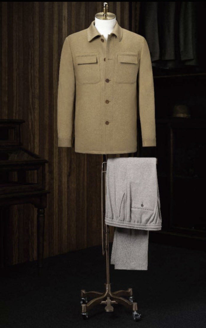 A tan camel casual jacket displayed on a mannequin with beige trousers, arranged on a wooden floor in a room with wooden panels.