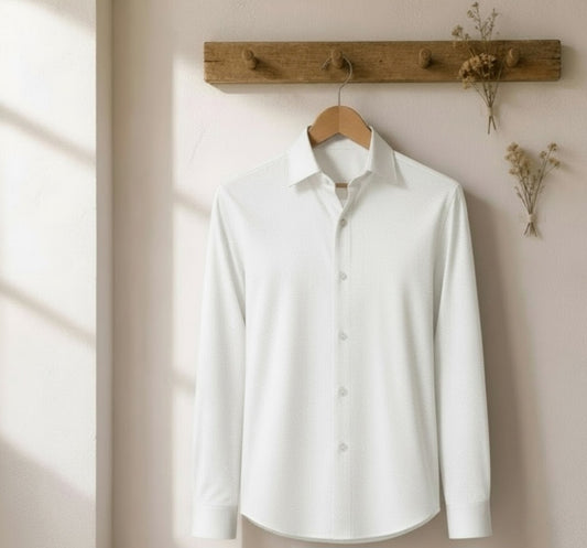 A white long-sleeve button-up dress shirt hanging on a wooden hanger from a rustic wooden wall rack, with dried floral decorations on a light beige wall.