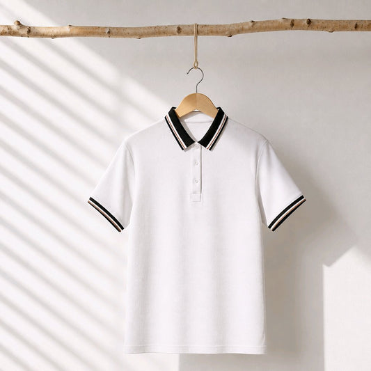 A white short-sleeve polo shirt with black and white striped collar and sleeve cuffs, hanging on a wooden hanger from a natural wood branch against a white wall with diagonal shadow patterns.