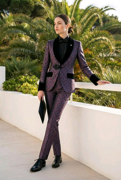 A woman models a purple and black patterned tuxedo suit with black lapels, paired with a black shirt and black dress shoes, standing on a white terrace with palm trees in the background.