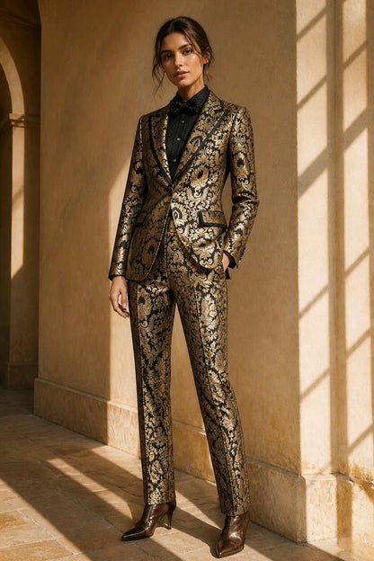 A woman stands in a sunlit architectural corridor wearing a tailored suit with an ornate black and gold patterned fabric, a black shirt, and brown pointed-toe heeled boots.