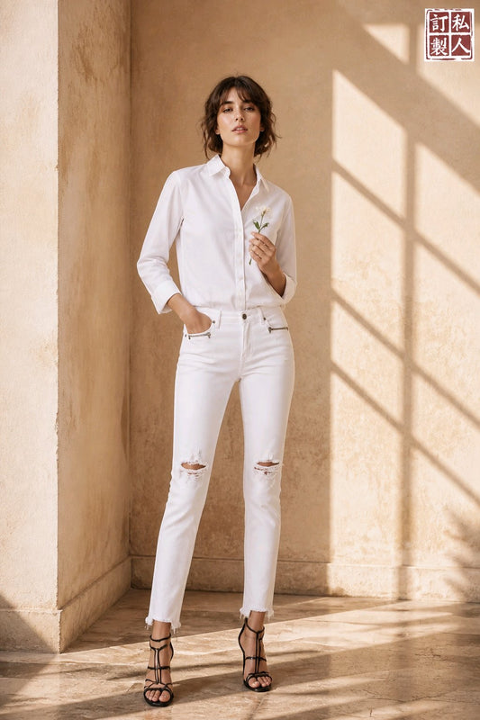 A woman stands in a sunlit beige interior wearing a white button-up shirt and white ripped jeans, with black strappy heels and holding a small white flower. A red logo with Chinese characters appears in the top-right corner.