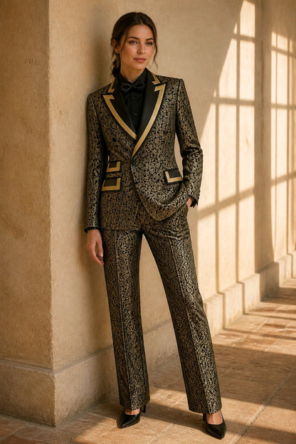 A woman stands in a sunlit stone corridor wearing a tailored two-piece suit with an ornate black and gold pattern, black lapels with gold trim, a black blazer, black trousers, a black shirt, and a black bow tie.