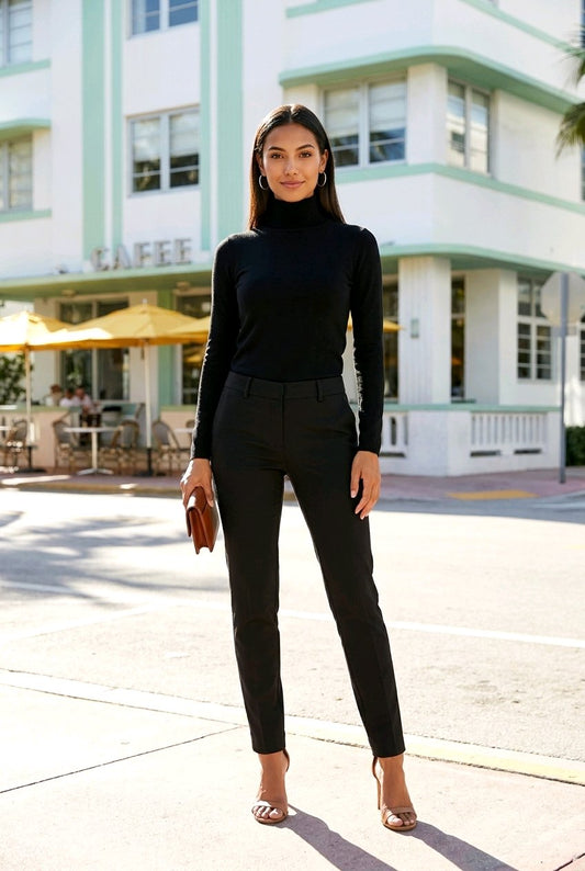 A woman stands on a sunny street wearing a black long-sleeve mock neck top and black slim-fit pants, paired with nude high heels and holding a brown clutch. A white and mint green cafe building is in the background.
