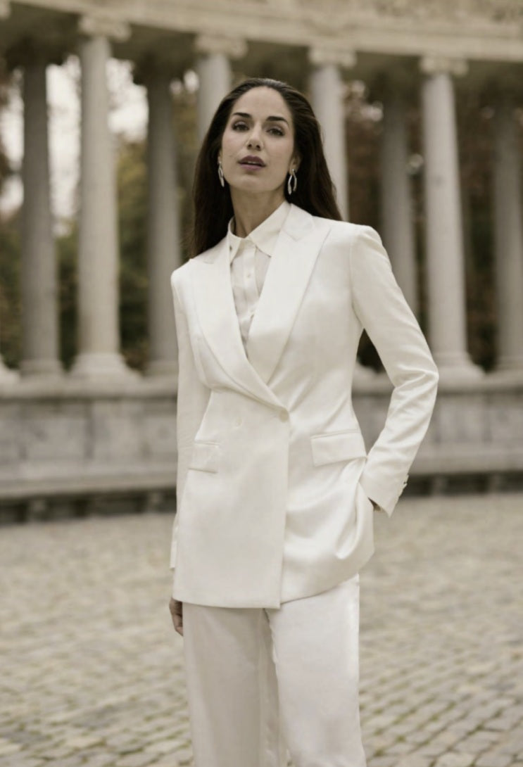 A woman wearing a white double-breasted, two-piece silk suit with a peaked lapel and straight flapped pockets.