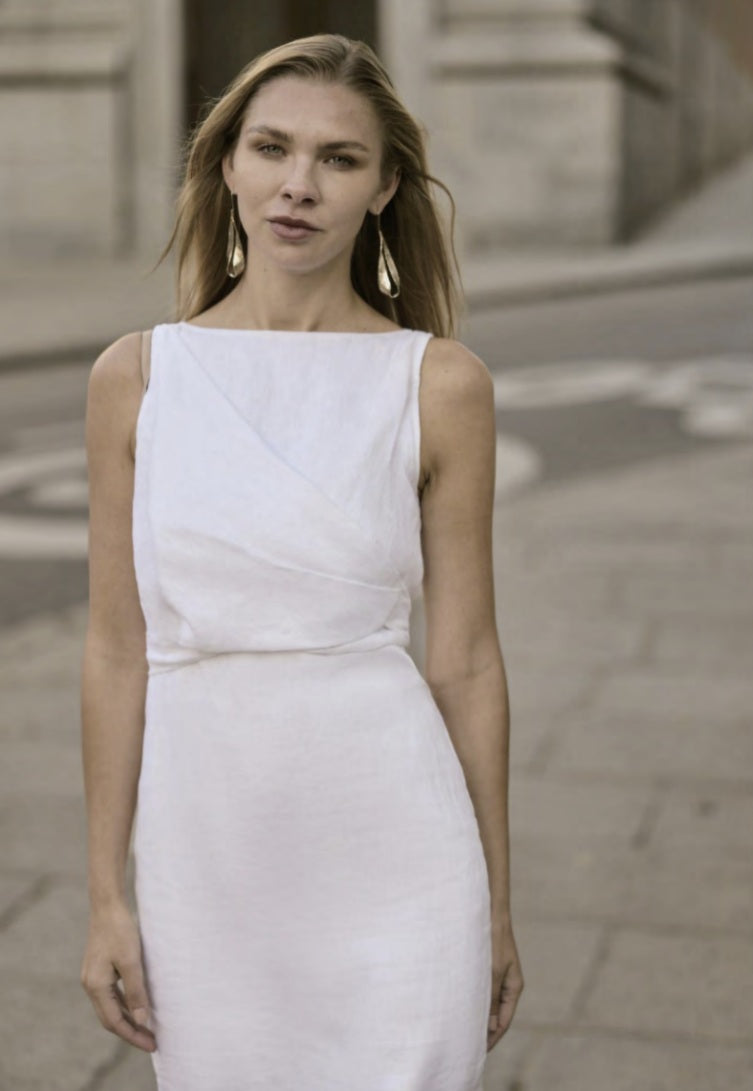 A woman wearing a white linen full dress with short sleeves and a square neckline.