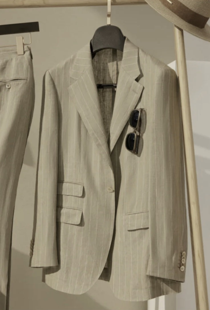 Beige pinstripe suit jacket on a hanger with sunglasses on top, against a neutral background.