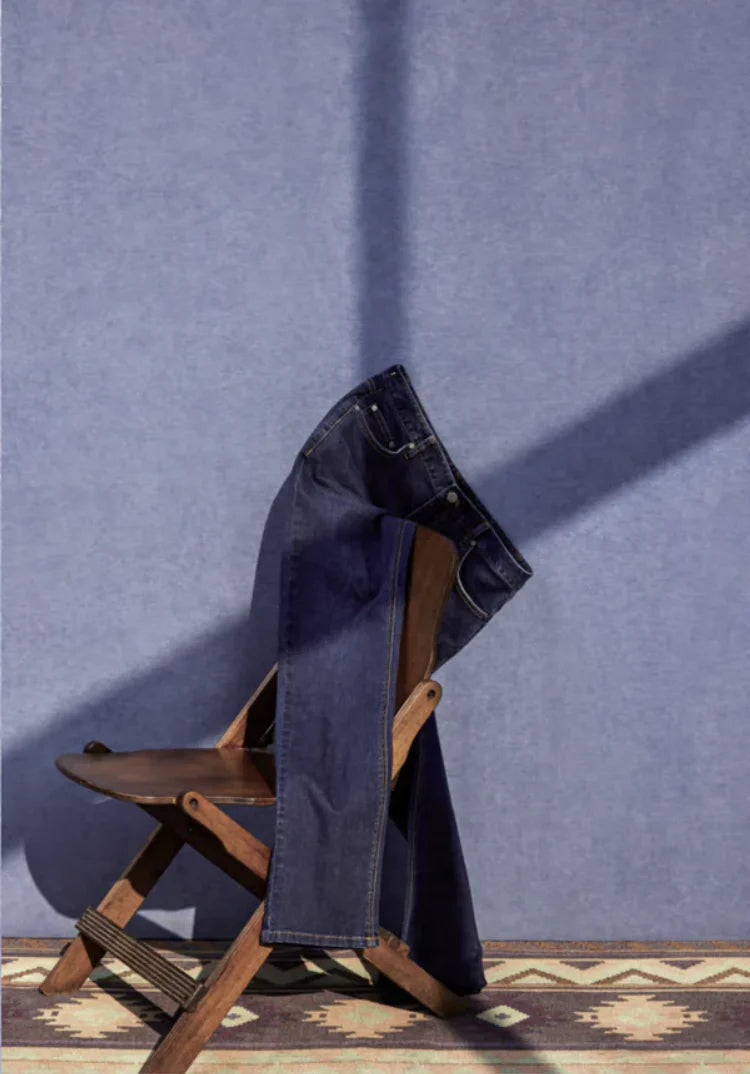Blue jeans draped over a wooden chair against a blue wall