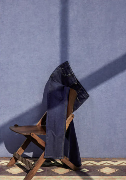 Blue jeans draped over a wooden chair against a blue wall