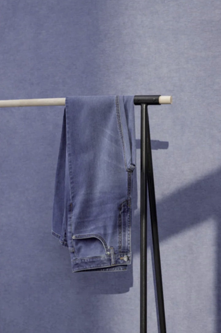 Blue jeans hanging on a black metal rack against a blue wall