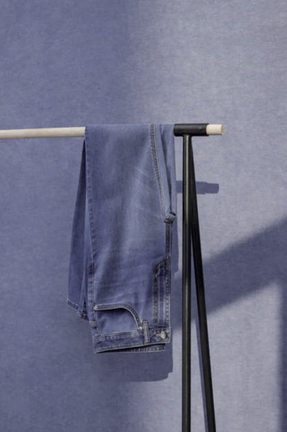 Blue jeans hanging on a black metal rack against a blue wall