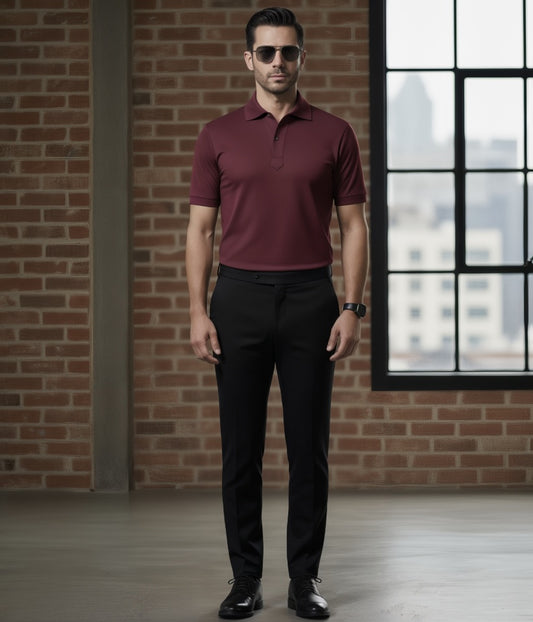 Man wearing a Burgundy polo shirt and black pants standing in front of a brick wall.