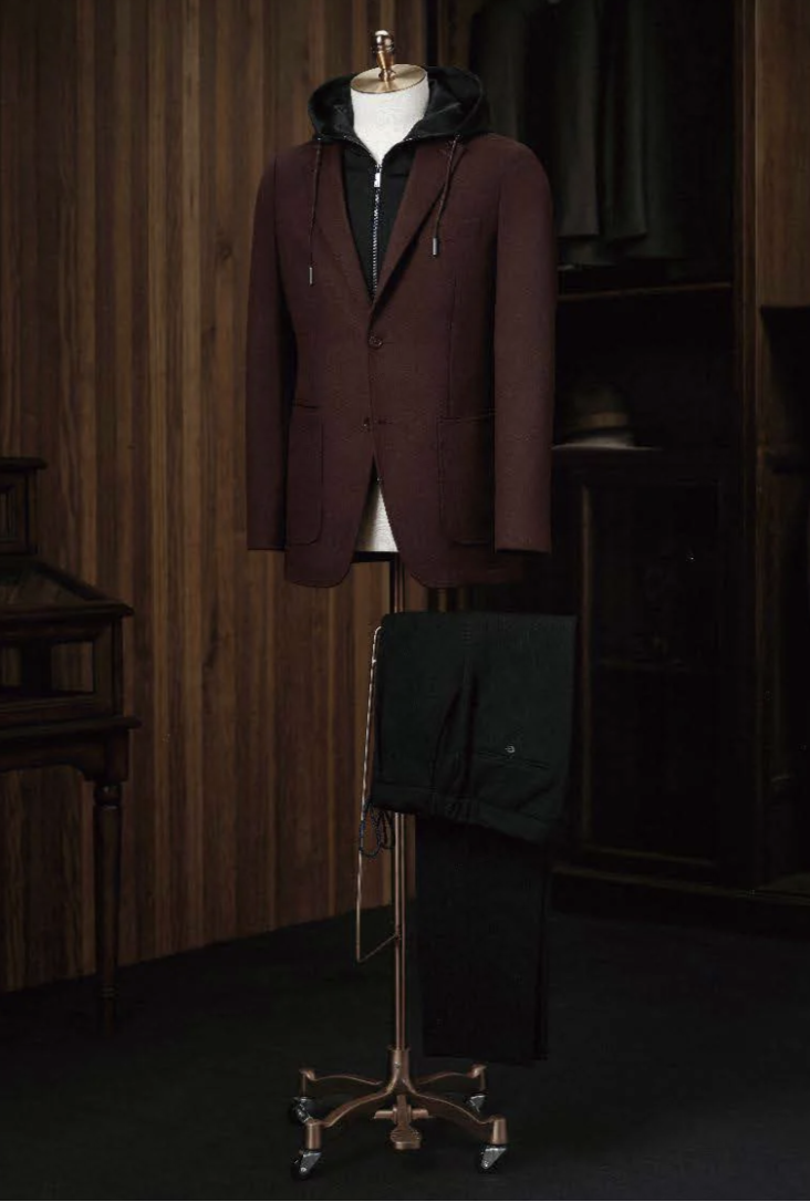 A burgundy check tweed jacket displayed on a mannequin with dark brown cord trousers, featuring a high shirt collar, front waistband, and cuffed sleeves.
