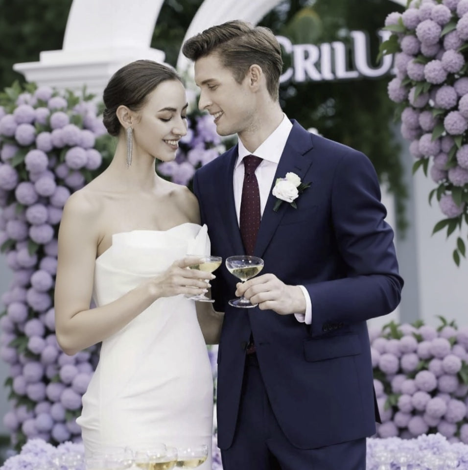 Couple in wedding attire holding glasses of champagne with a floral backdrop