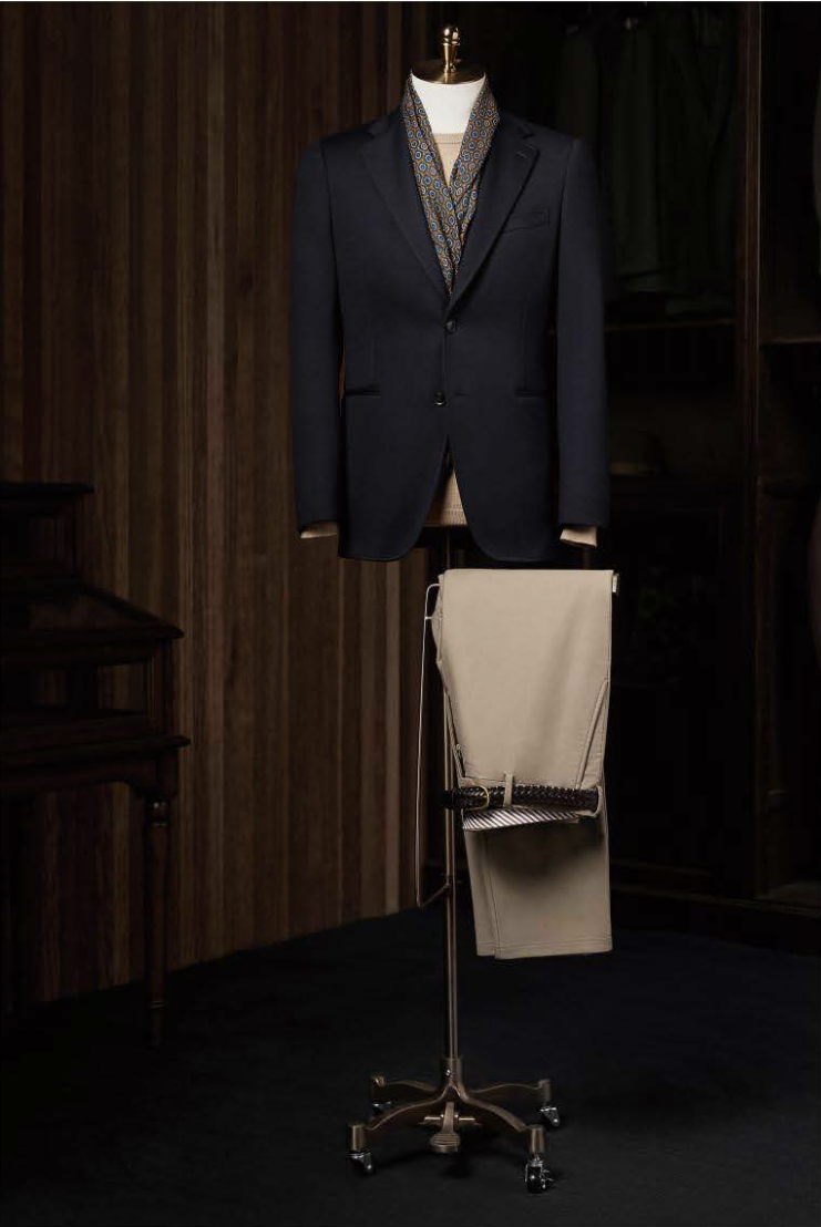 A dark navy casual blazer on a mannequin and a pair of stone trousers displayed separately on a stand, set against a background of a wood-panelled room.