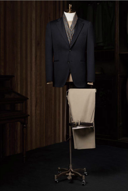 A dark navy casual blazer on a mannequin and a pair of stone trousers displayed separately on a stand, set against a background of a wood-panelled room.