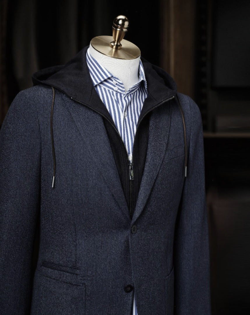 Dark blue coat on a mannequin with a striped shirt underneath against a dark background