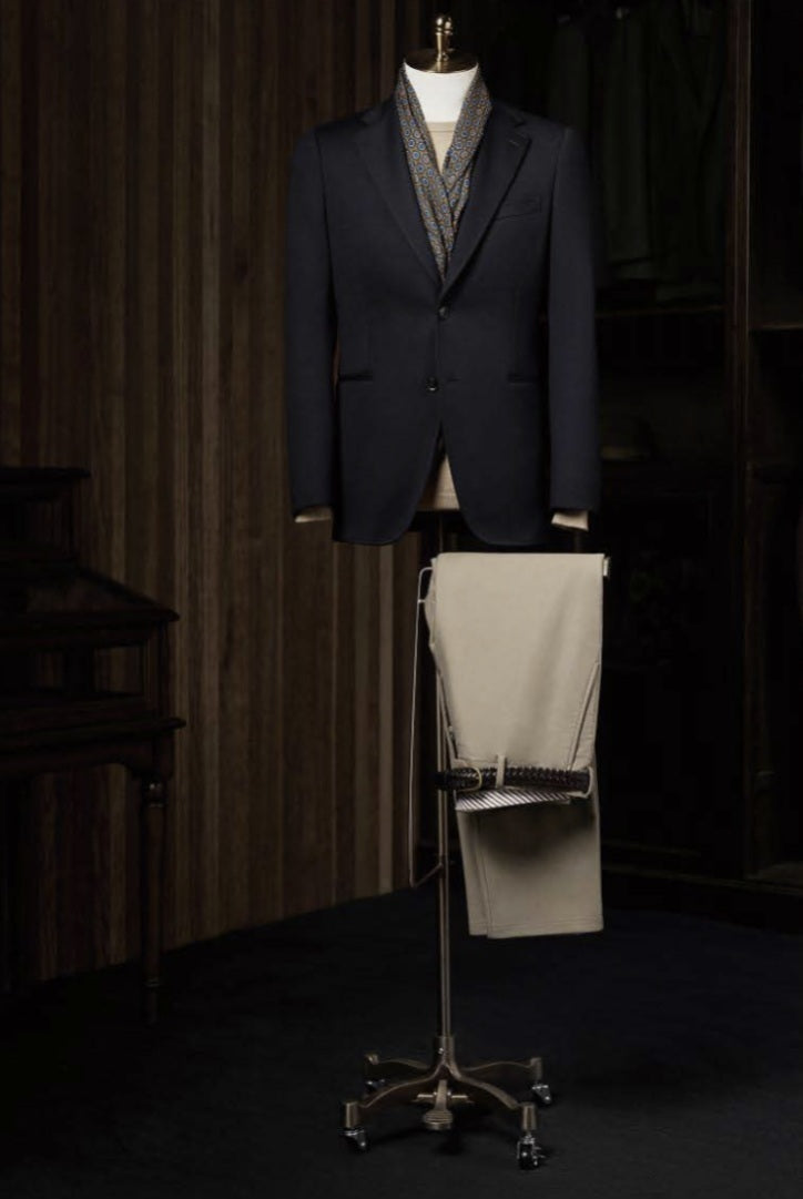 Dark suit jacket on a mannequin with a light-colored shirt and tie against a dark background