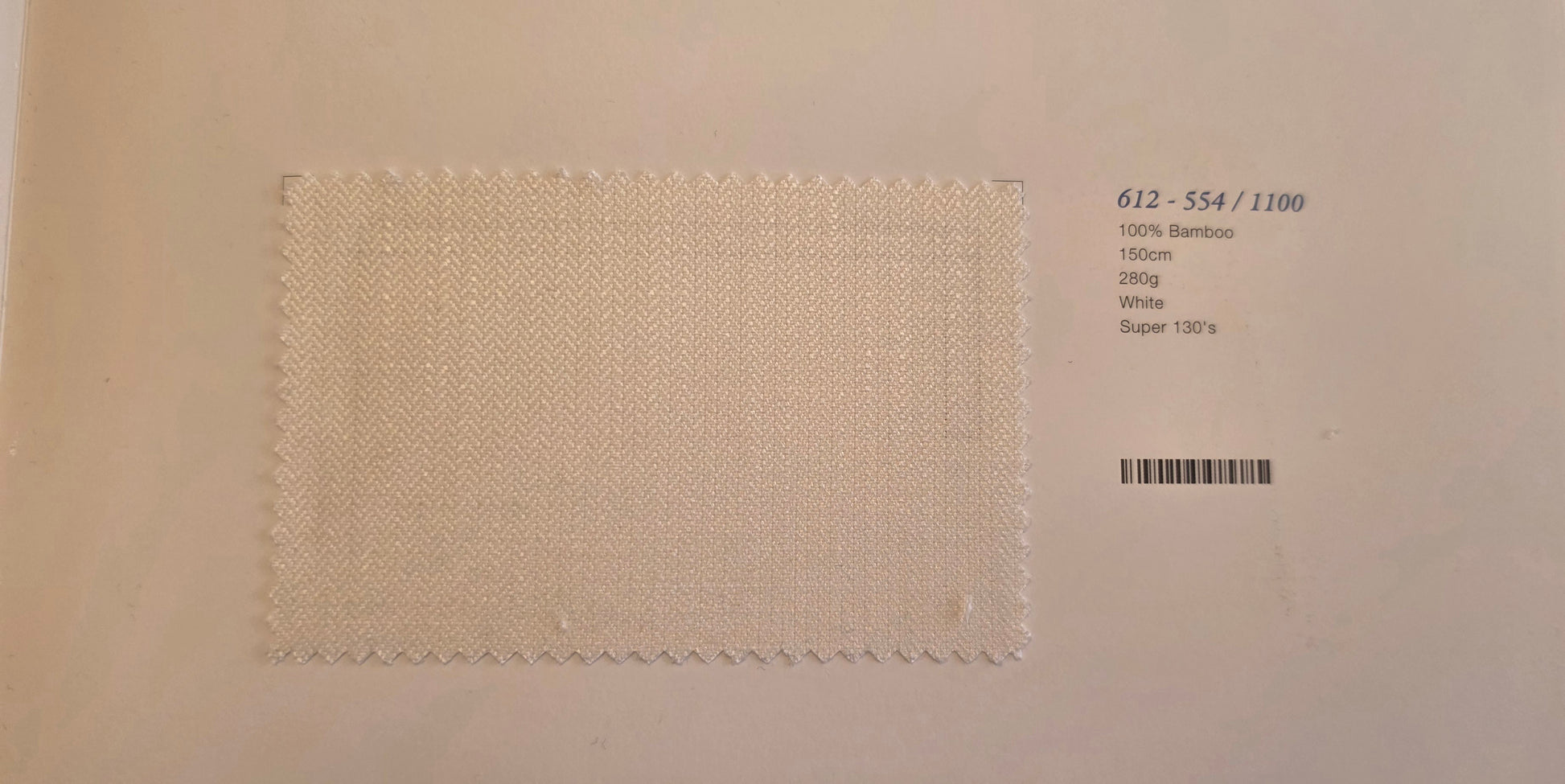 A square fabric swatch of off-white woven material with a zigzag stitched border, displayed on a light beige background next to printed product details including a barcode and text '612 - 554 / 1100'.