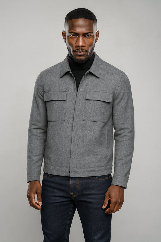 Man wearing a gray jacket and dark jeans against a plain background