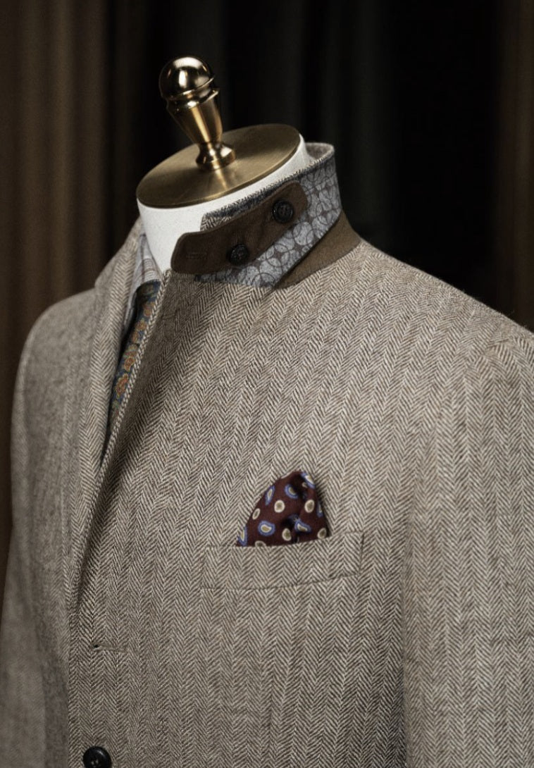 Grey textured suit jacket with patterned shirt and pocket square on a mannequin against a dark background
