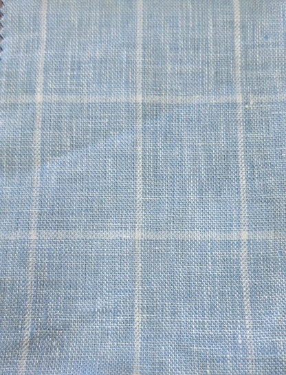 A close-up of light blue woven fabric with a subtle white windowpane plaid pattern.