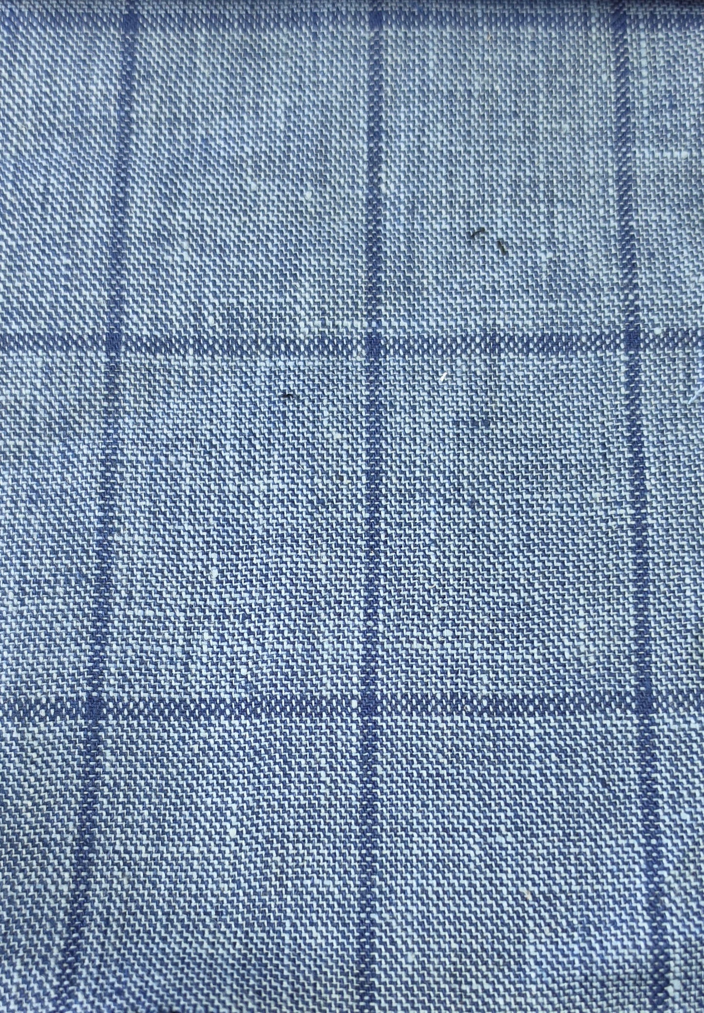A close-up of a blue woven fabric with a subtle windowpane plaid pattern.