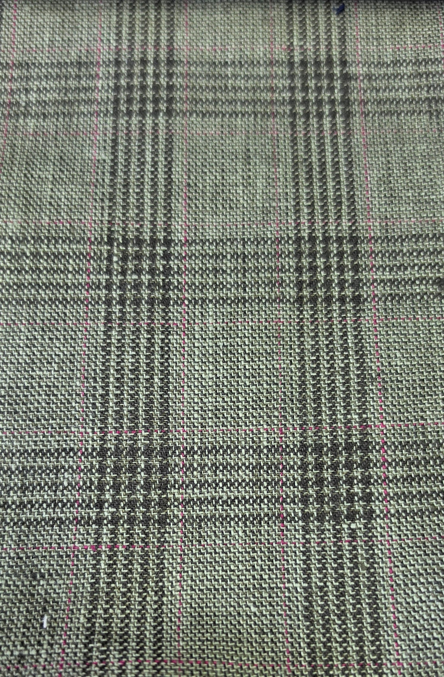 A close-up of woven fabric with a small-scale plaid pattern in olive green black, overlaid with faint pink measurement grid lines.