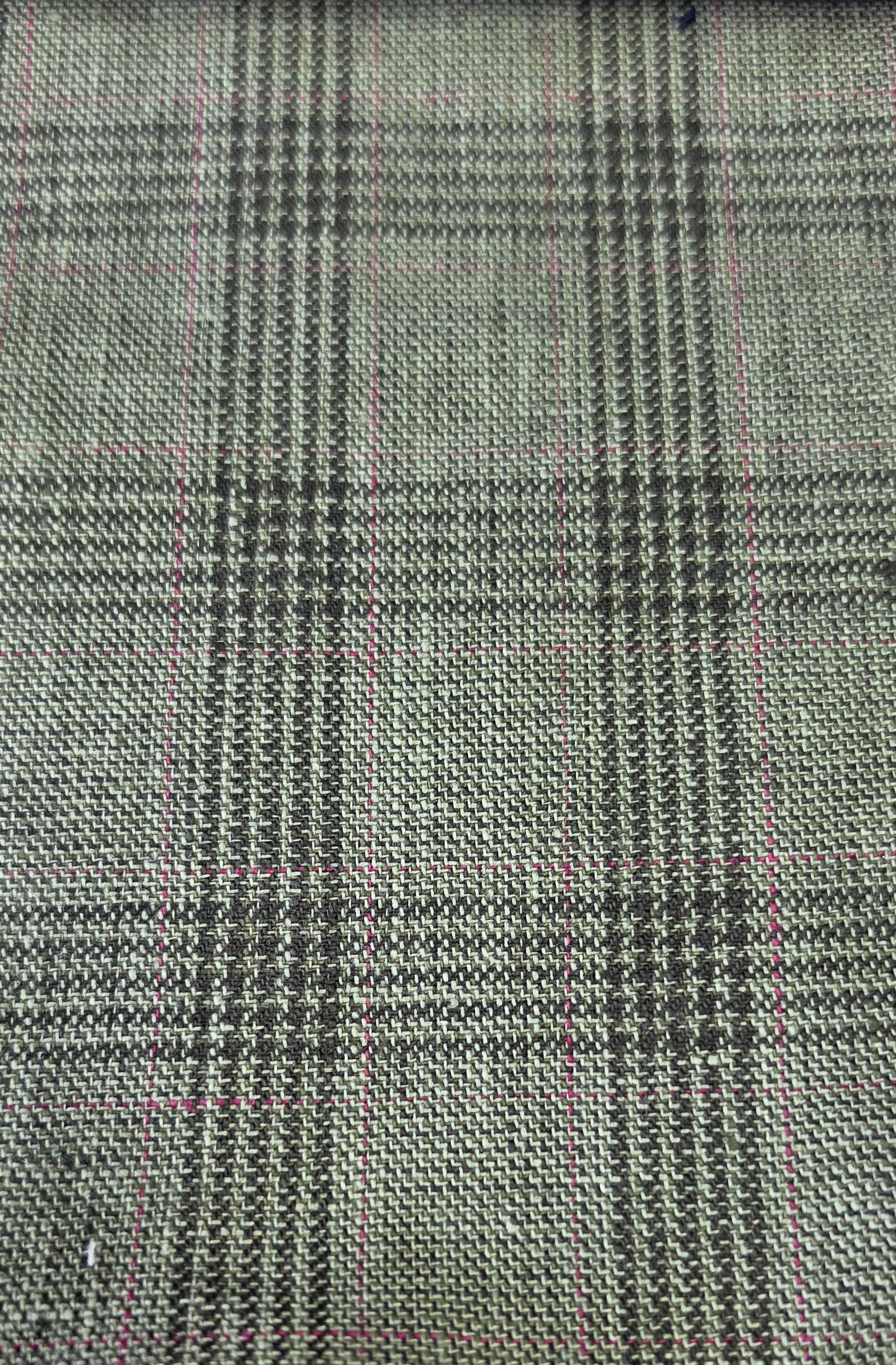 A close-up of woven fabric with a small-scale plaid pattern in olive green black, overlaid with faint pink measurement grid lines.